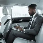 Businessman Working on Laptop in Back Seat of Luxury Car