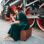 Woman sitting on suitcase against steam train