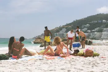 front view of multi ethnic group of friends relaxing and enjoying at beach on a sunny day while men holding cooler