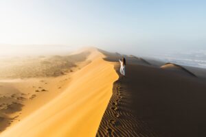 Woman enjoying sunrise on top of huge sand dune. Beautiful warm sun light and mist in morning. Sahara desert, Morocco.