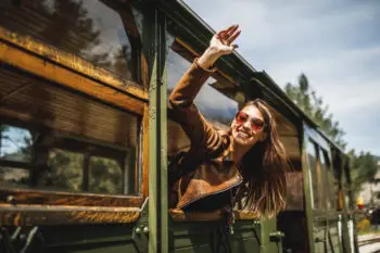 A smiling young woman looking and waving through a window while traveling by a retro train.